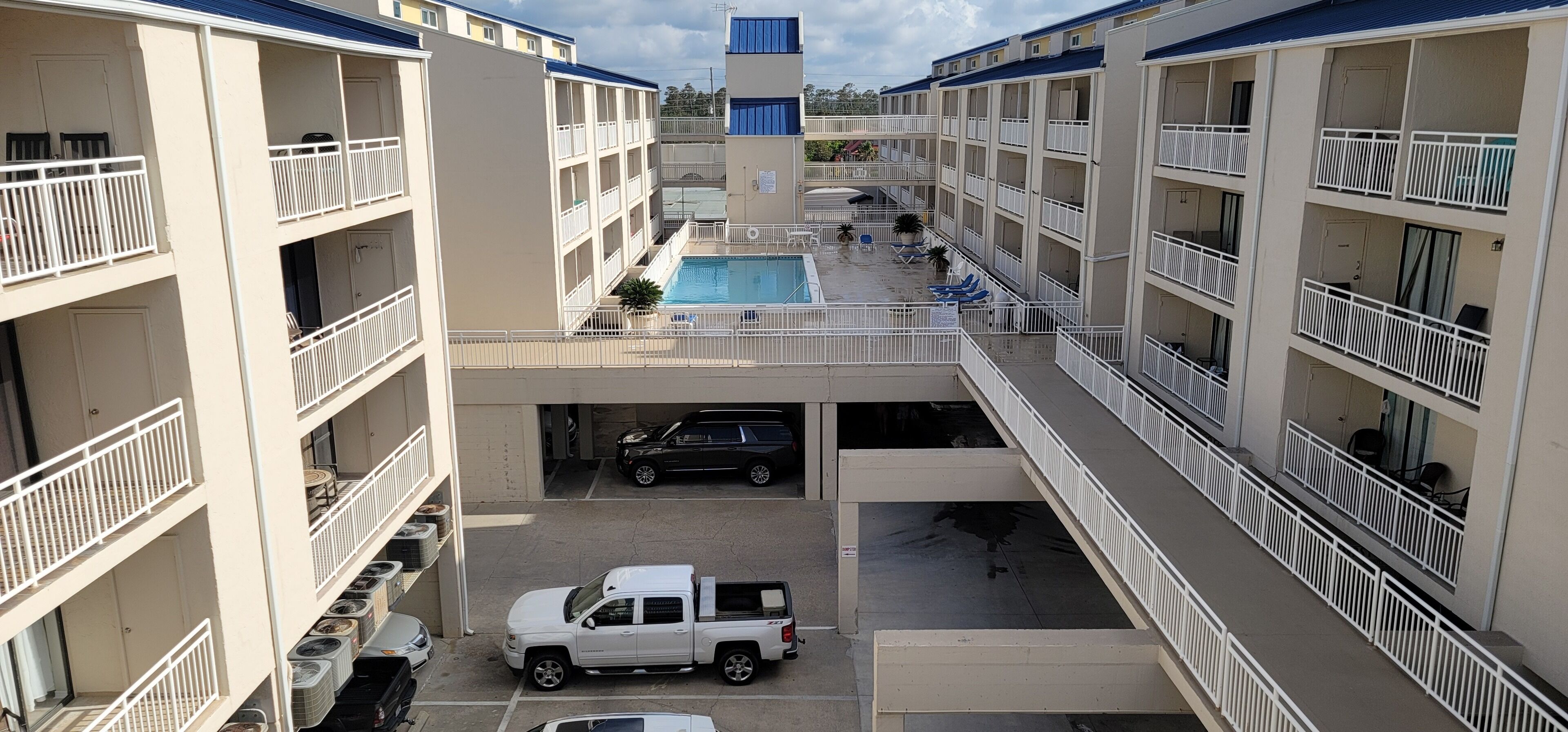 A multi-story hotel with a central pool, balconies, and a parking area.