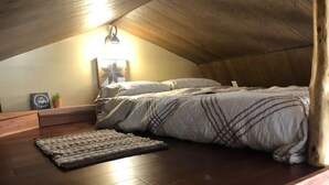Un dormitori d'altell acollidor, amb sostre de fusta, un llit amb estoreta estampada, una catifa petita i un lluminari fixat a la paret.