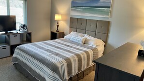 Une chambre à coucher avec un lit, une télévision, une lampe et un tableau représentant l’océan.