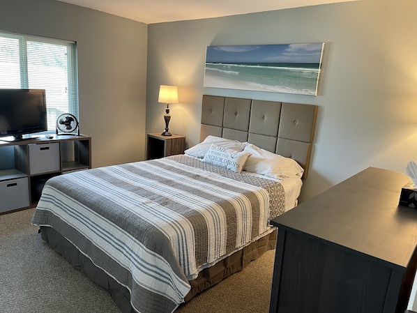 Een slaapkamer met een bed, een televisie, een lamp en een schilderij van de zee.