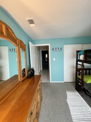 Een slaapkamer met een houten dressoir, een stapelbed, een spiegel en een gang die naar een andere kamer leidt.