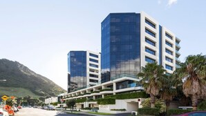 Ein modernes Hotel mit Glasfassade, mehreren Balkonen und einem angelegten Garten.