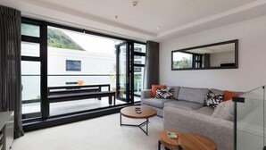 Ein modernes Wohnzimmer mit einer Couch, zwei Couchtischen und einem großen Fenster mit Blick auf einen Balkon und ein Gebäude.