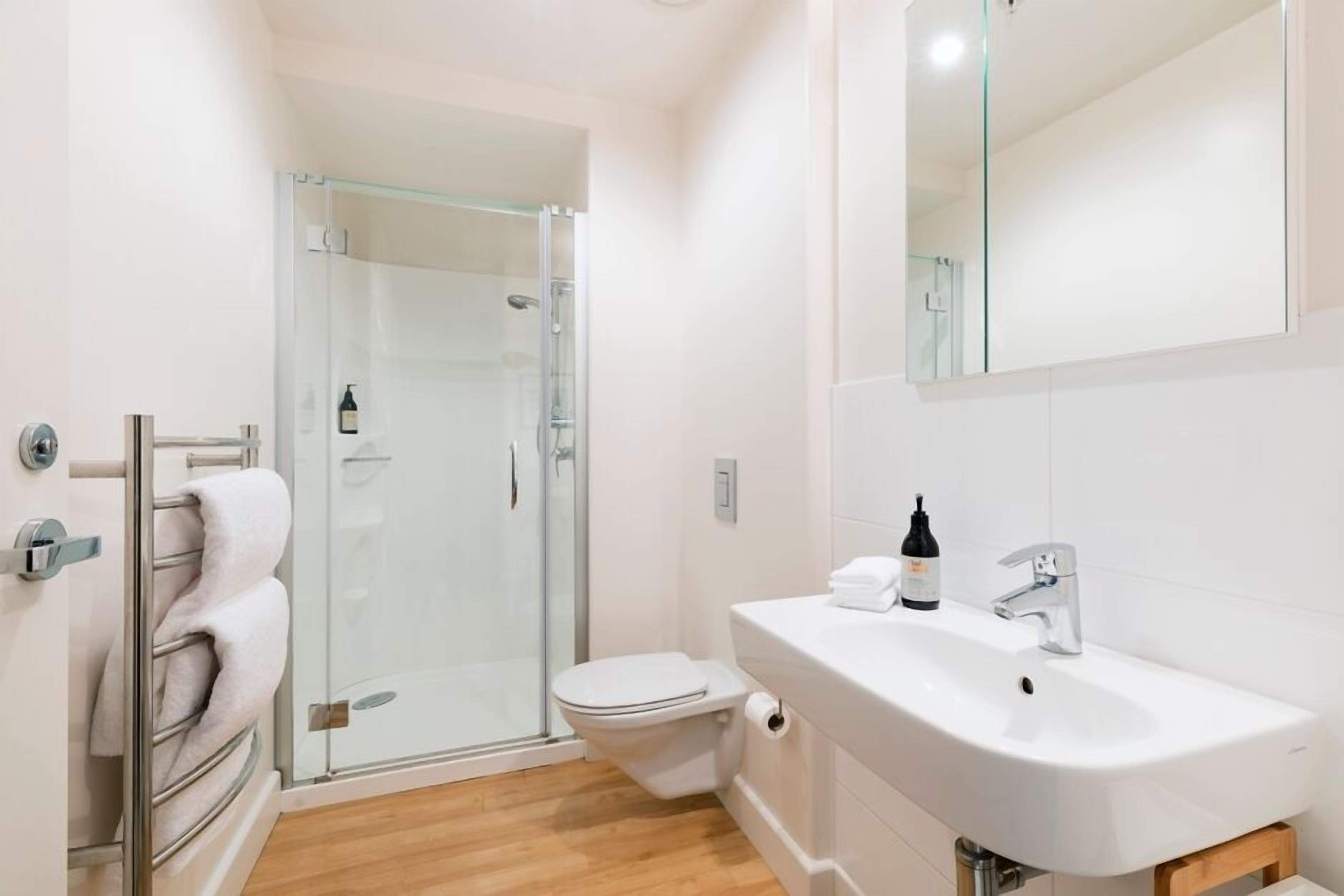 A modern bathroom with a glass shower enclosure, a toilet, and a sink with a mirror above.