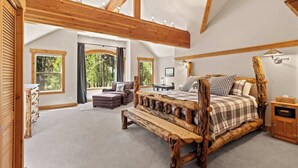 A bedroom with a large bed, wooden beams, and a view of greenery.