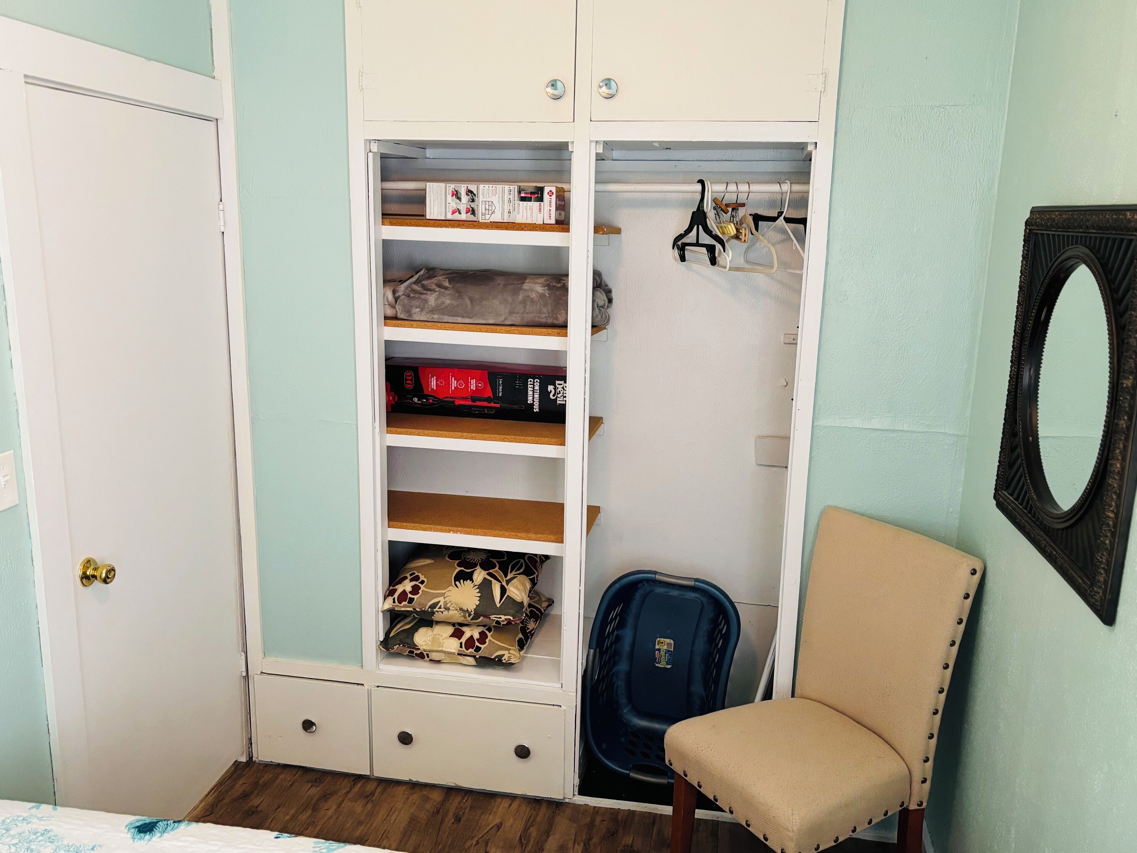 A bedroom with a wardrobe, a chair, and a mirror.