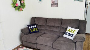 Un sofá marrón con dos almohadas, un tapete floral y adornos de pared que incluyen un lazo, un pez y letreros con motivos de cabaña.