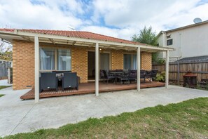 A covered patio with outdoor furniture, a brick house, and a wooden deck.
