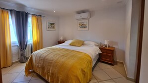 Ein Schlafzimmer mit einem Bett, Vorhängen, einem Heizkörper, einer Wand-Klimaanlage und zwei Nachttischen mit Lampen.