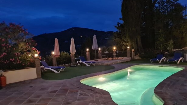 Ein Swimmingpool mit Liegestühlen und Sonnenschirmen, umgeben von einer Pflasterterrasse und viel Grün.