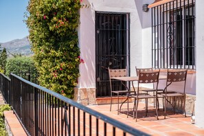 Un balcón con una mesa y sillas, baranda de metal negro y un edificio blanco con una puerta negra.