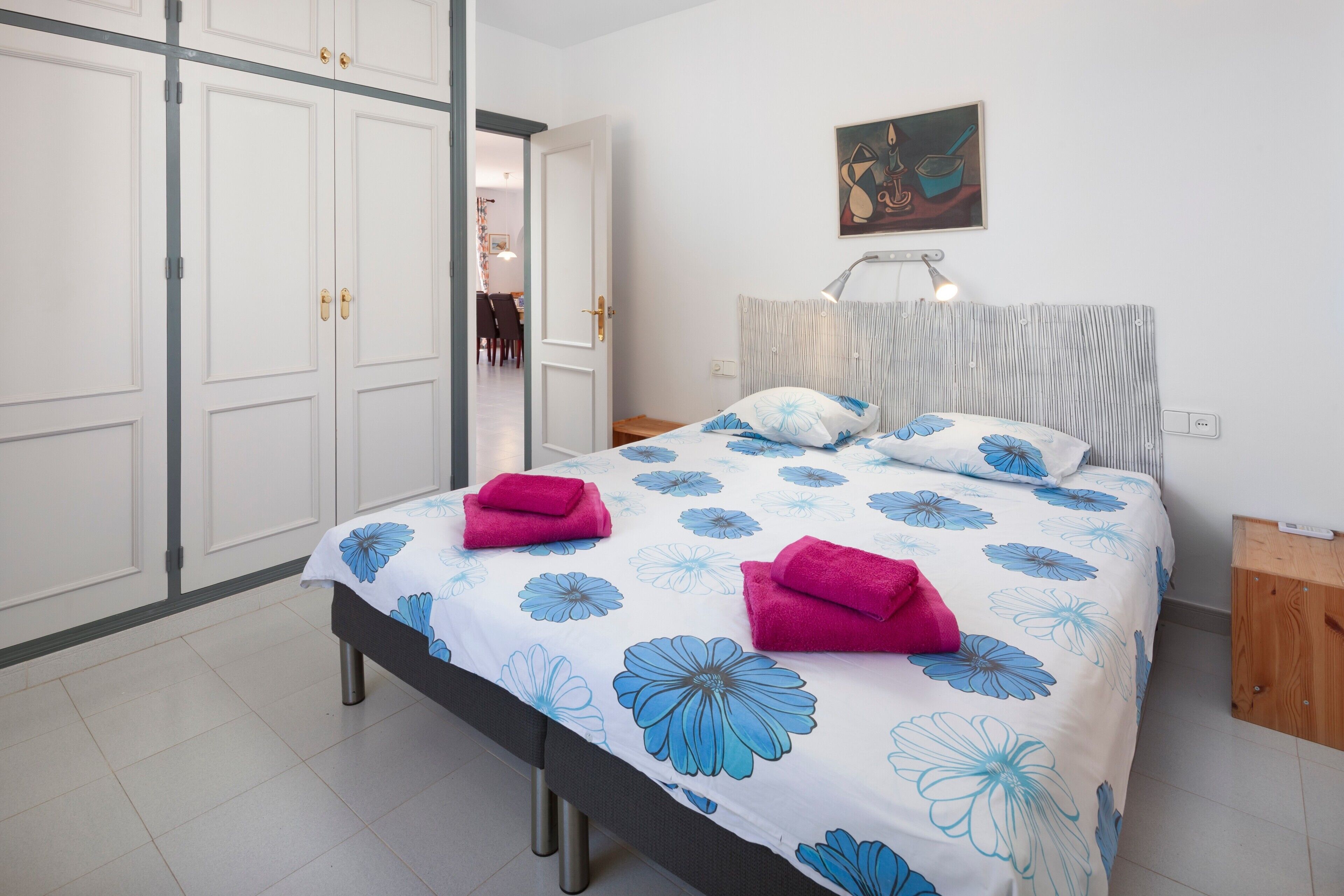 Quarto com cama, mesa de cabeceira, luminária, quadro e guarda-roupa.