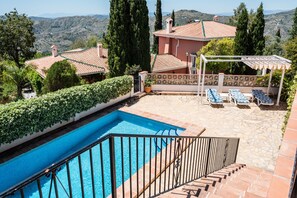 Una piscina con barandilla metálica, una pérgola con sillones de descanso y vistas del paisaje circundante.