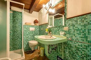 Een badkamer met een groene mozaïektegelwand, een wit toilet, een groene wastafel en een douche.