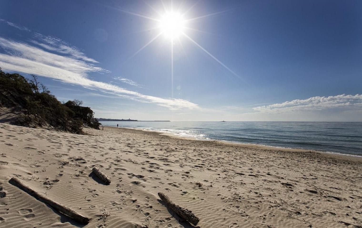 Ein sandiger Strand mit Fußabdrücken, ein klarer Himmel und die strahlende Sonne.