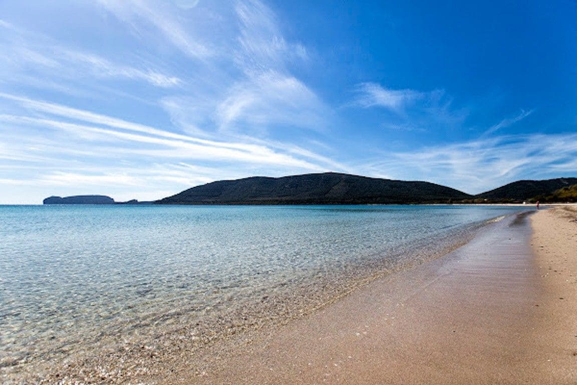 Een strand met helder water, een zandstrand en heuvels in de verte.