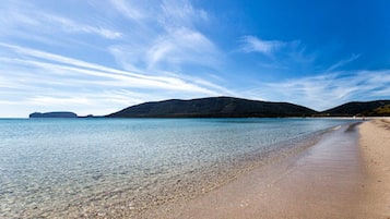 Een strand met helder water, een zandstrand en heuvels in de verte.
