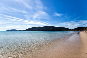 Een strand met helder water, een zandstrand en heuvels in de verte.