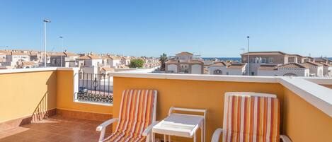 Terraza en la azotea con dos sillones a rayas y una pequeña mesa, con vista a un barrio residencial de tejados de terracota.