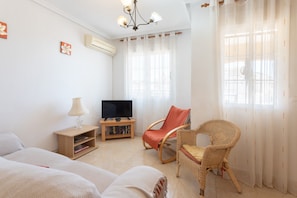 Um quarto com uma cama, uma televisão sobre um suporte, uma cadeira de vime e uma estante.