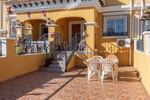 Um edifício amarelo com um pátio ladrilhado, uma escadaria e uma mesa com cadeiras.