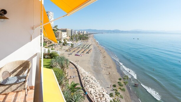 Un balcón con toldo amarillo que da a una playa con cielo despejado.