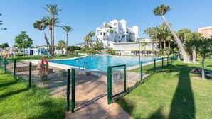Una piscina rodeada por una valla, con palmeras y un edificio al fondo.
