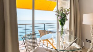 Un balcón con una mesa de vidrio, sillas de mimbre, un jarrón con flores y vista al mar.
