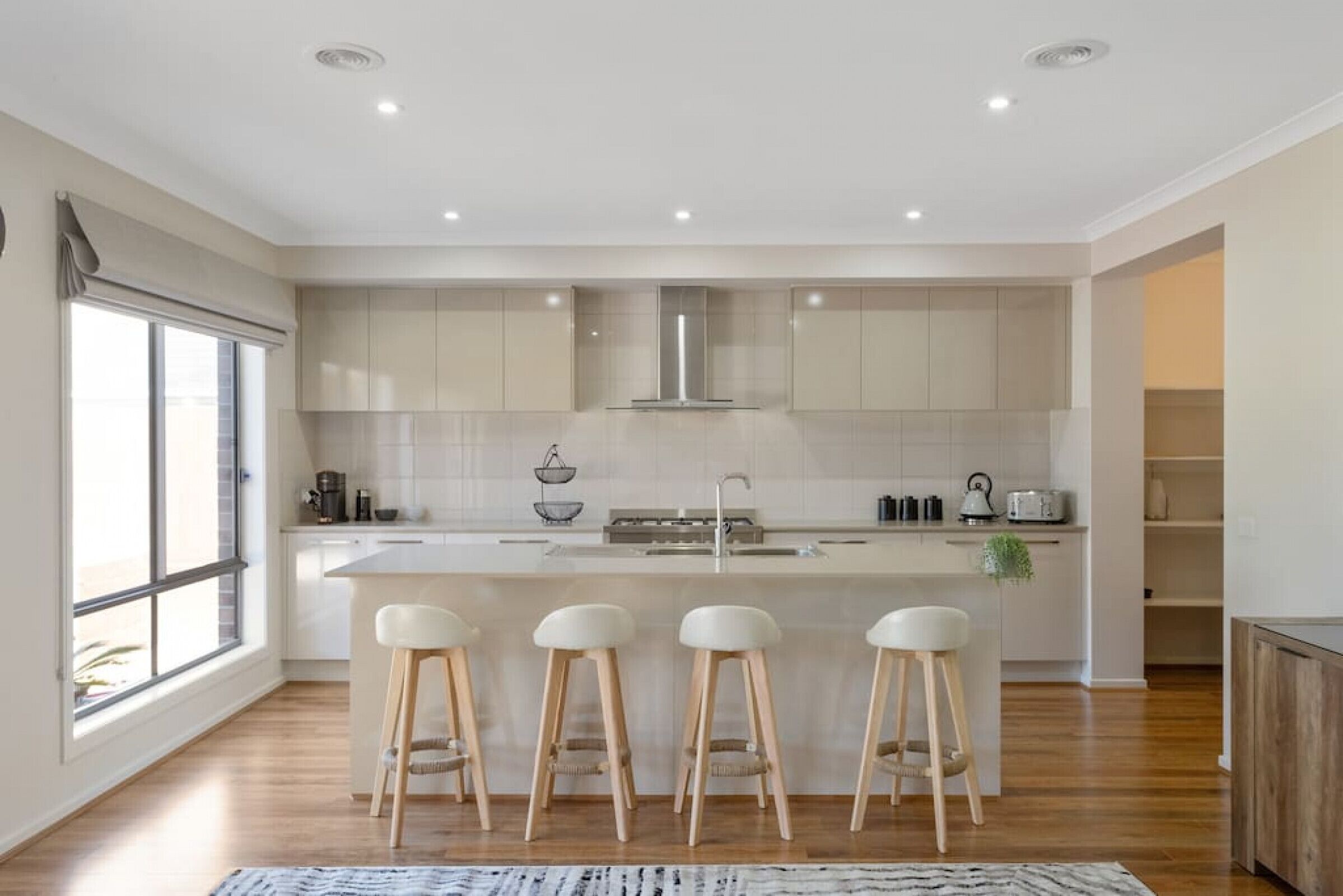 A modern kitchen with a central island, bar stools, and a large window.