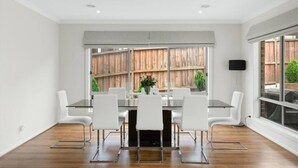 A modern dining area with a glass table and white chairs, a wooden fence view, and a large window. - Seagrove Escape - Near the beach & WIFI (Cowes)