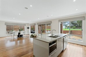 A modern kitchen with a central island, large windows, and a view of the outdoors. - Seagrove Escape - Near the beach & WIFI (Cowes)