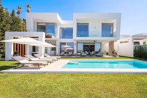 A modern two-story house with a swimming pool, outdoor seating, and a clear view of the sky.