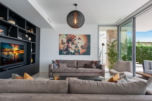 A modern living room with a sofa, a large painting, and a hanging light fixture.