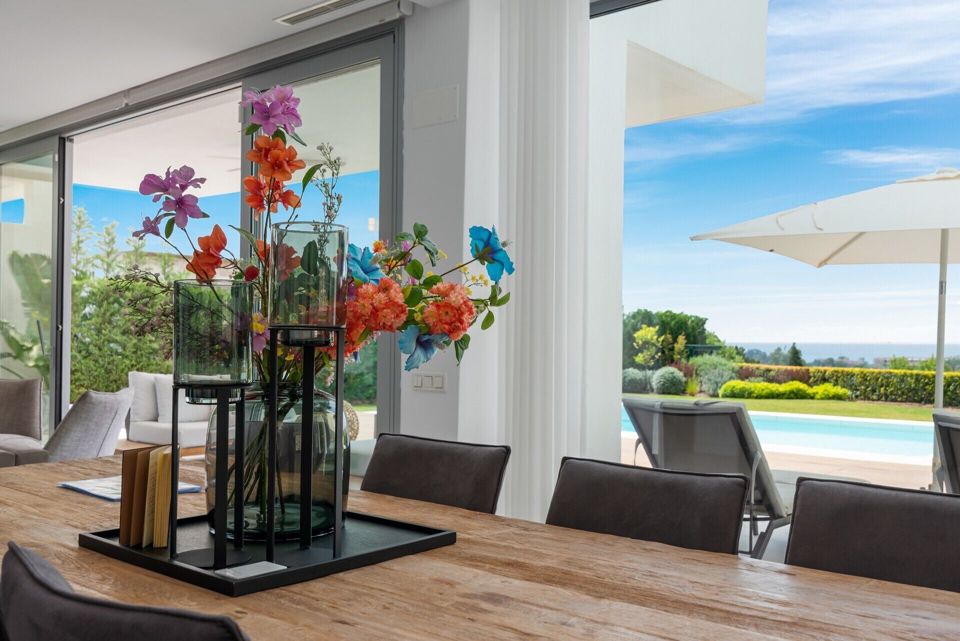 A dining area with a wooden table, chairs, and a glass vase with flowers.