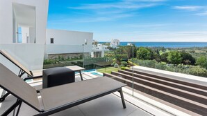 Una terrazza esterna moderna con piscina, poltrona a sdraio e vista sul mare e sugli edifici circostanti.