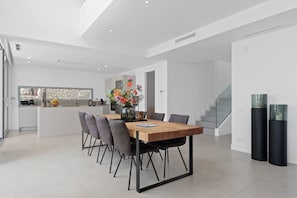 A modern dining area with a wooden table and chairs, a kitchen in the background, and a staircase.