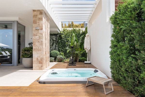 A modern outdoor hot tub area with a wooden deck, exercise equipment, and lush greenery.
