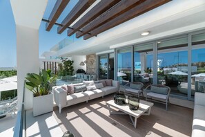A modern outdoor living area with a sofa, chairs, a coffee table, and a large window overlooking a scenic view. - Villa 'Riva' with Sea Views, Wi-Fi and Air Conditioning (Marbella)