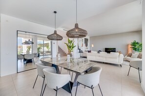 A modern living room with a glass-top dining table, white sofas, and wicker pendant lights. - Villa 'Riva' with Sea Views, Wi-Fi and Air Conditioning (Marbella)