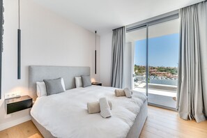 A modern bedroom with a large bed, bedside tables, and a view of a cityscape through floor-to-ceiling windows. - Villa 'Riva' with Sea Views, Wi-Fi and Air Conditioning (Marbella)
