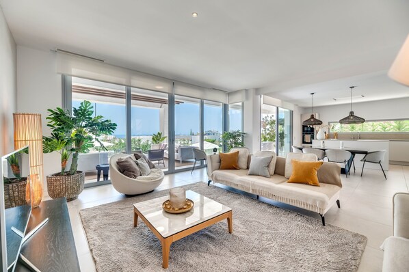 A spacious living area with a sofa, coffee table, and large windows offering a view of the outdoors. - Villa 'Riva' with Sea Views, Wi-Fi and Air Conditioning (Marbella)