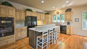 A kitchen with wooden cabinets, a central island with bar stools, a refrigerator, an oven, and a clock on the wall. - Private Dock & Pool Access! Hot Springs Home (Hot Springs)