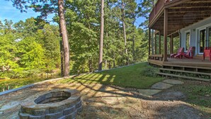 A wooden deck with red chairs, a stone fire pit, and a view of a forested area. - Private Dock & Pool Access! Hot Springs Home (Hot Springs)