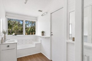 A bathroom with a white sink, a window with a view of trees, and a door. - Moonah Cottage Rye by Ready Set Stay- Close to the beach & WIFI (Rye)