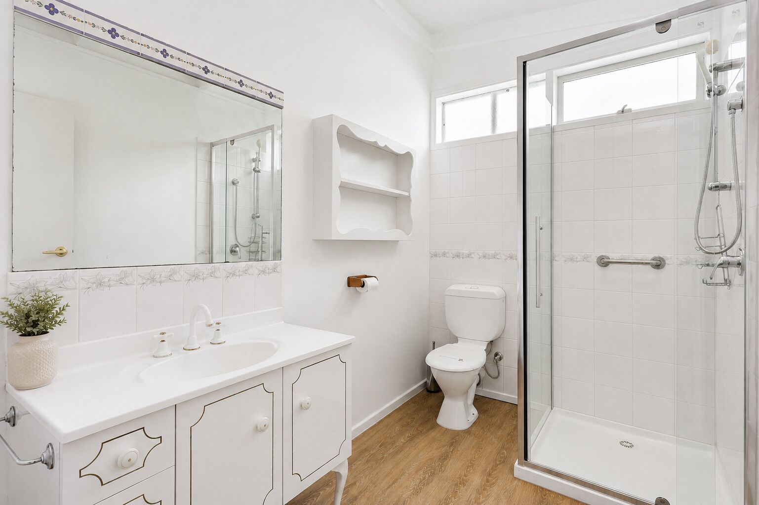 A bathroom with a white sink, a toilet, a shower enclosure, and a mirror.