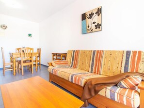A living room with a sofa, wooden chairs, a coffee table, and a wall-mounted artwork.