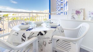 Un balcón con mesa lista para comer, sillas blancas y vistas a edificios al fondo.