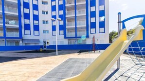 Un parque infantil con un tobogán amarillo frente a un edificio azul y blanco con varios balcones.