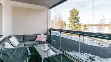 A balcony with a glass table, a grey sofa with cushions, and a view of a snowy landscape.