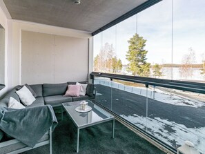 Un balcon avec une table en verre, un canapé gris agrémenté de coussins et une vue sur un paysage enneigé.